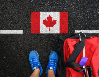 a man with a shoes and travel bag is standing on asphalt next to flag of Canada and border