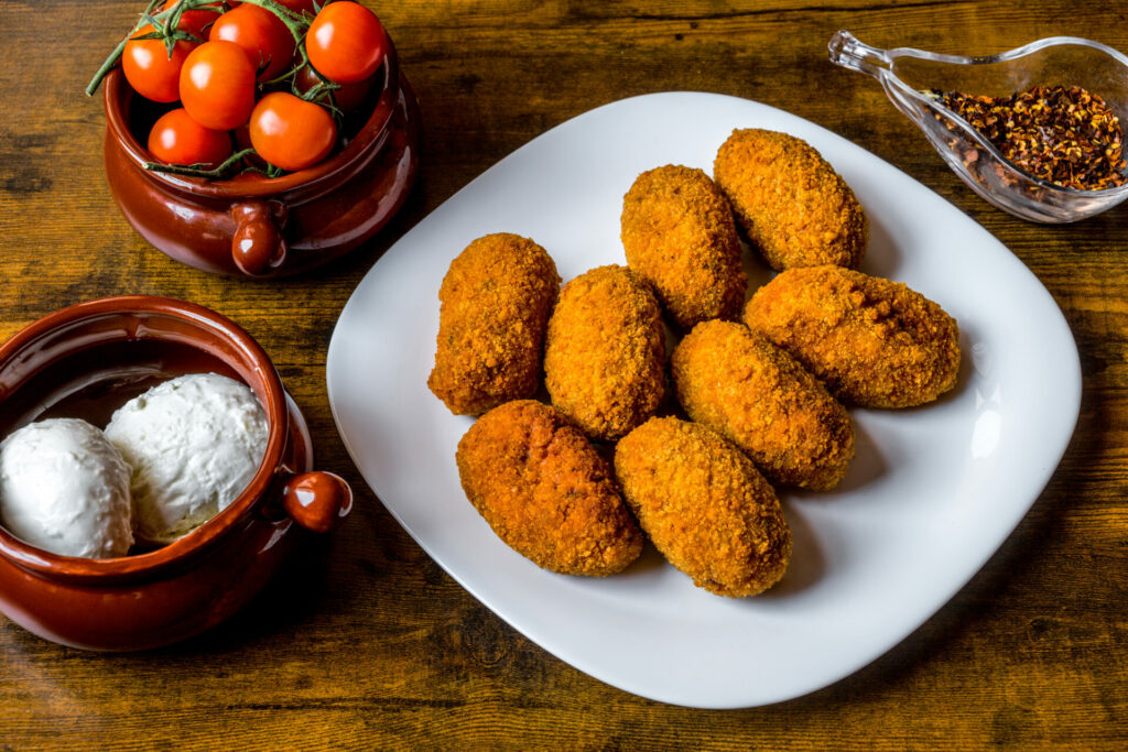 A plate of delicious and crunchy Suppli al Telefono, usually sold to take away. This famous Italian dish is made up of breaded and fried rice balls. The rice is seasoned in tomato sauce, sometimes in meat sauce, and stuffed with mozzarella. The result is a crunchy snack to eat while walking or as an appetizer. A peculiarity of this gastronomic tradition is the name itself: the indication of Suppli al Telefono (Croquette at Telephone) is due to the mozzarella filling, which once bitten, stretches to form a thread, as if it were a vintage telephone. In 2017 the art of Italian pizza was declared by UNESCO as an Intangible Cultural Heritage. Image in High Definition format.